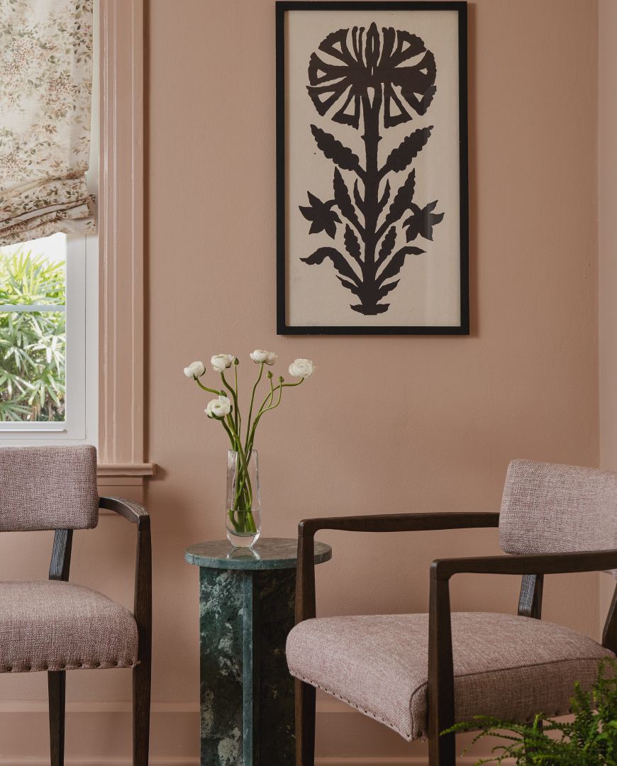 Two chairs and a marble side table against a blush wall