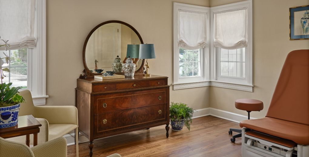 A sunlit exam room with an antique dresser and a bay window