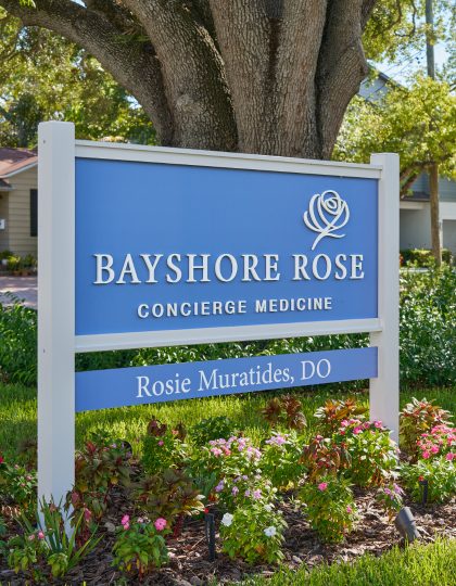 The blue Bayshore Rose Concierge Medicine sign beneath an oak tree